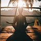 Person meditating at sunrise in tropical outdoor setting, seated cross-legged on yoga mat with palms up, surrounded by palm trees and warm sunlight—symbolizing mindfulness, tranquility, and nature connection.